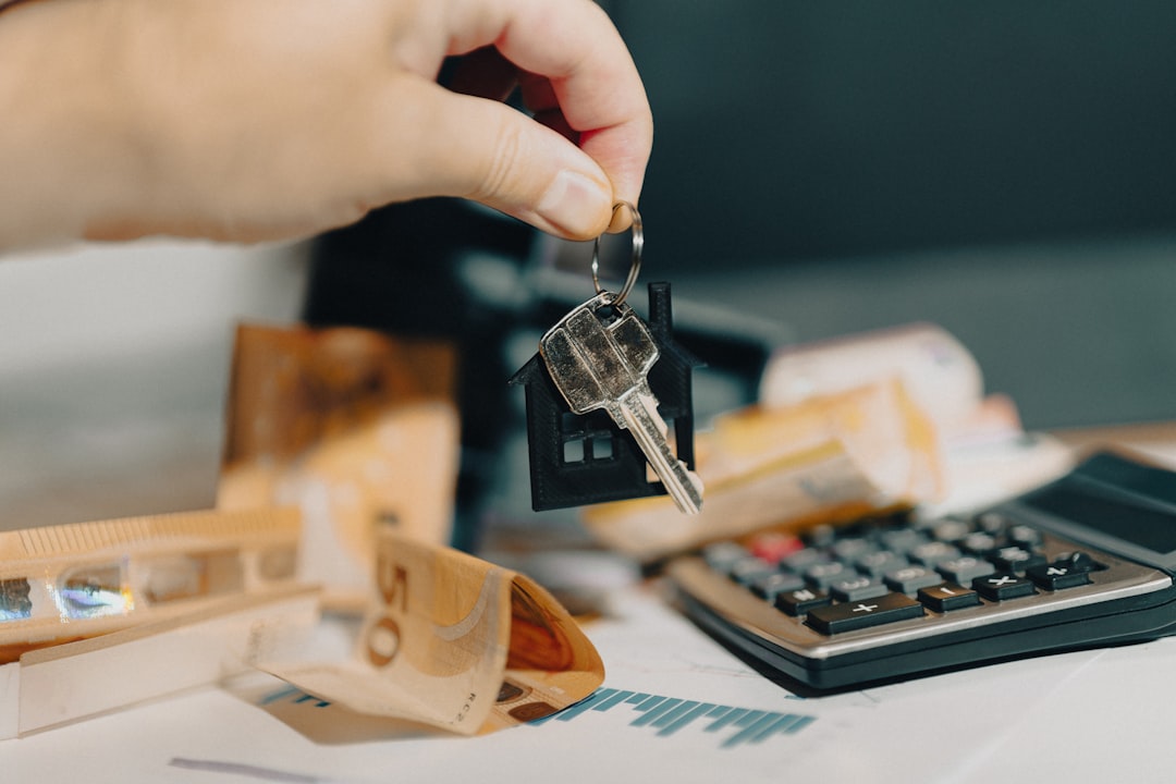 Main tenant une clé de maison sur des billets et une calculatrice.
